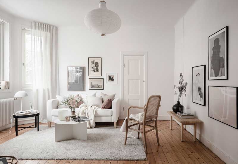 Salón con parquet, silla y banco de madera y paredes, alfombra, cortinas y sofá de color blanco