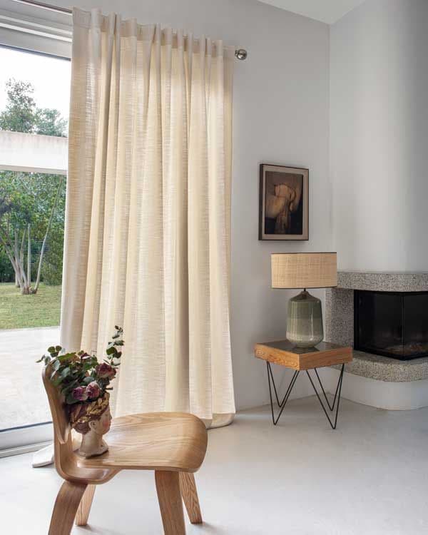 Salón con chimenea con salida al jardín con corredera de cristal y cortina beis con barra metálica