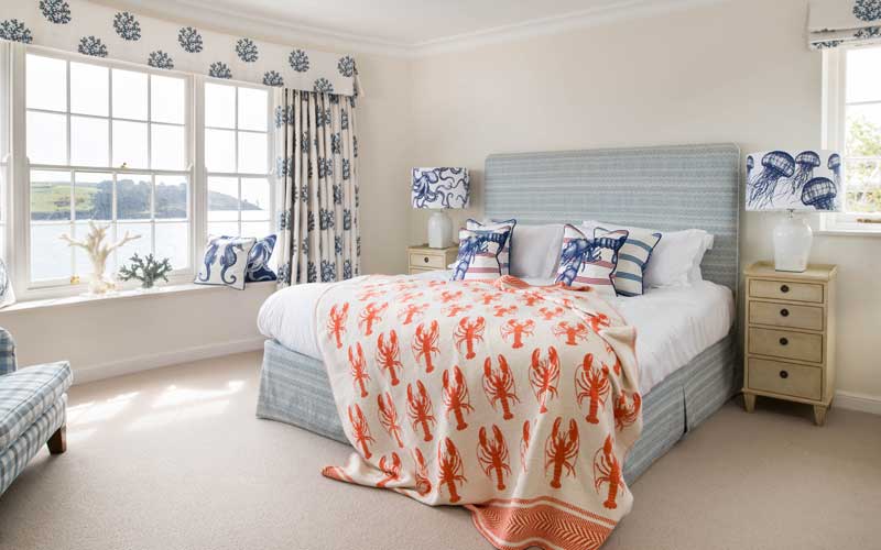 Dormitorio de matrimonio con gran ventanal, cabecero tapizado y cortinas con bandó a juego con corales en color azul