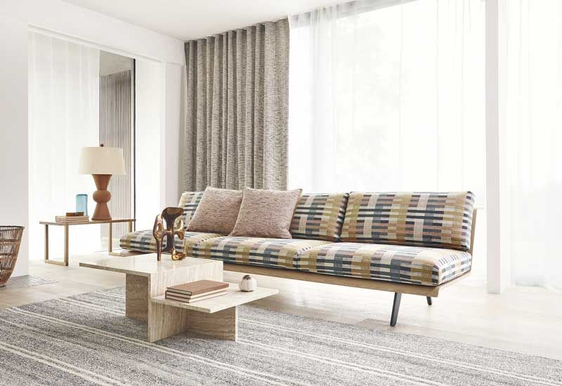 Salón con sofá de motivos geométricos y ventanas con cortinas y visillos 