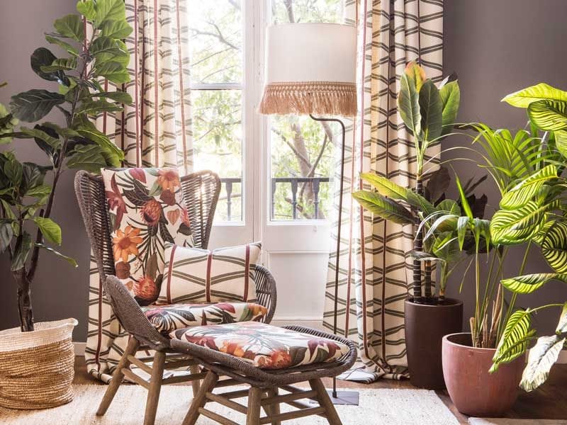 Rincón de lectura con plantas, butaca con puf a juego y cortinas de motivos geométricos
