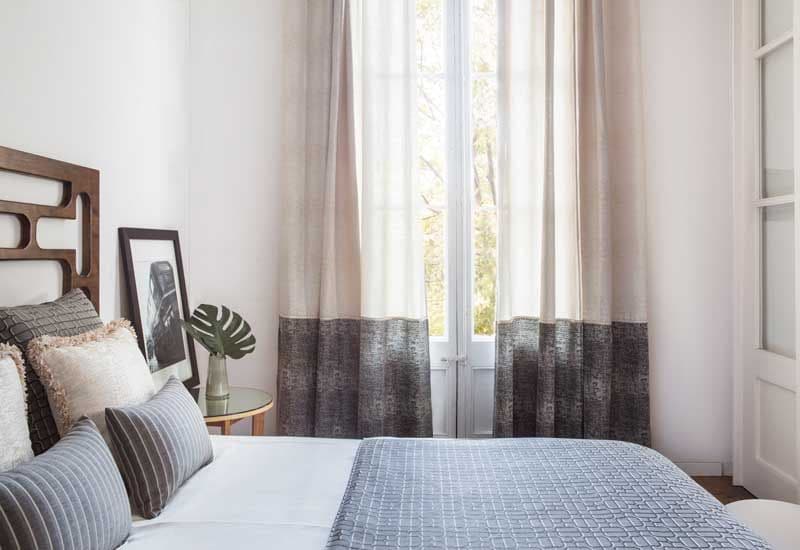 Dormitorio con cama con cabecero de madera y cortinas beis con una franja inferior gris