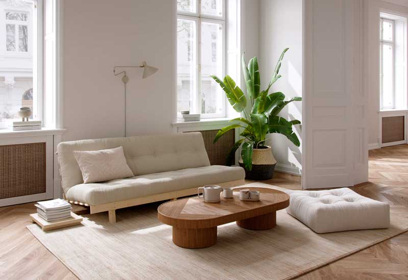 Salón en tonos claros con sofá blanco, mesa de centro de madera, puf y alfombra de fibras vegetales