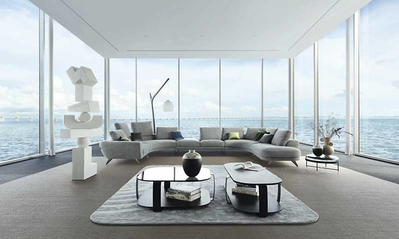 Saló modern amb envans de vidre amb vistes al mar amb sofà gris XL, dues taules de centre i catifa 