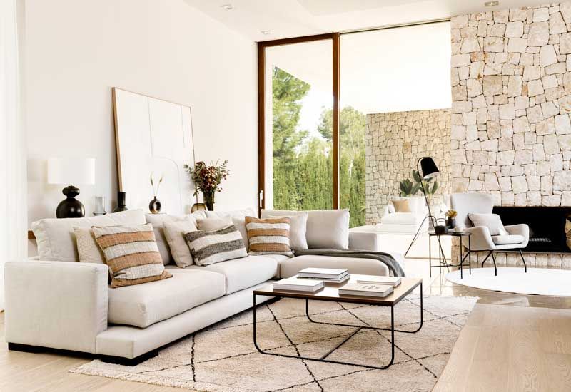 Salón con chimenea con pared de ladrillo, sofá blanco con chaise longue, cuadro y alfombra con motivos geométricos