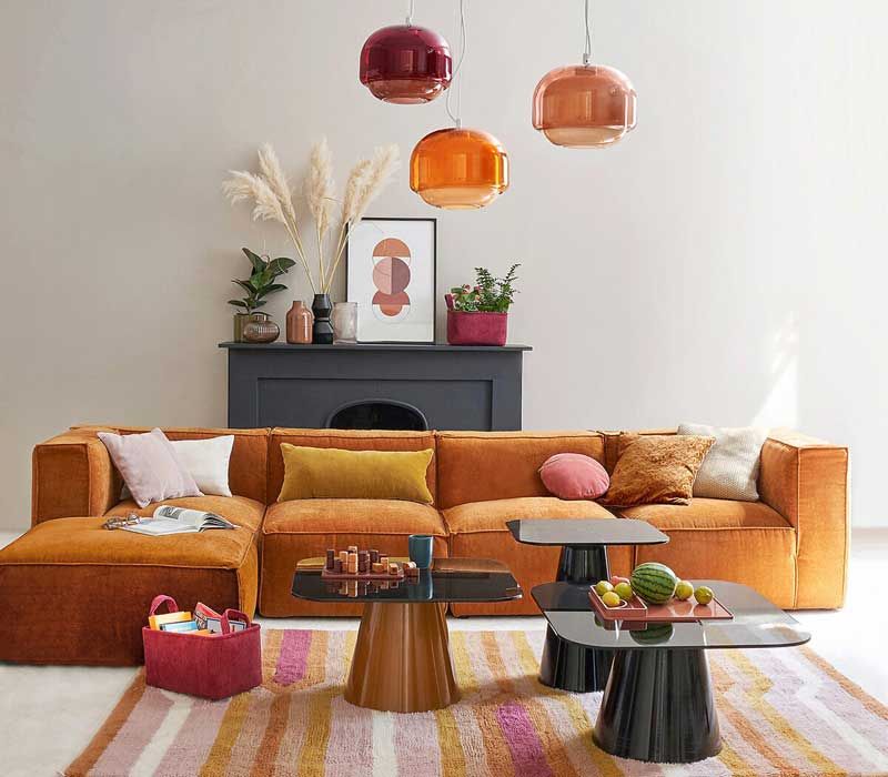 Salón con chimenea, lámparas de techo y alfombra de colores y sofá con chaise longue en mostaza