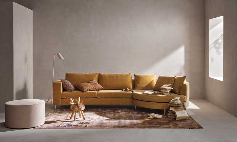Salón con paredes en color piedra, sofá mostaza con alfombra marrón