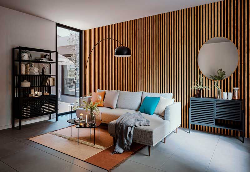 Salón con pared revestida con lamas de madera, sofá gris, alfombras en tonos marrones y lámpara de pie tipo Arco