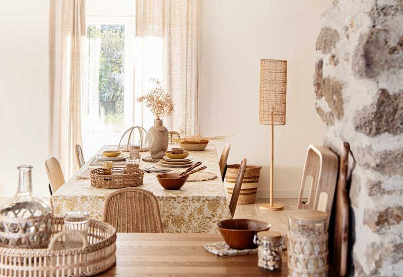 Comedor con cortinas beis y mesa vestida con mantel de hojas en tonos claros, muebles de