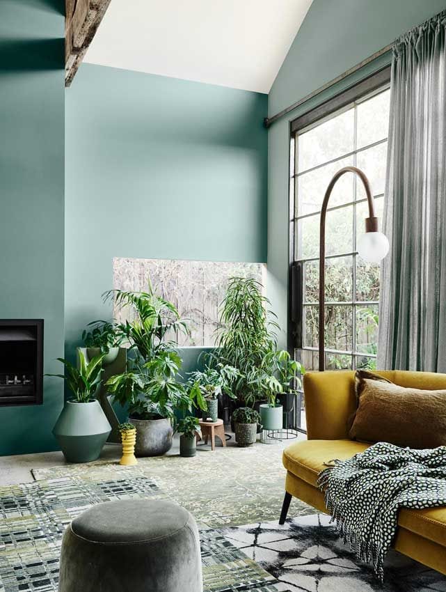 Salón decorado en verde con plantas y sofá amarillo