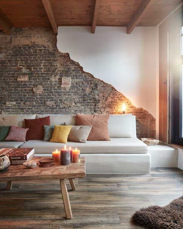 Salón con pared de ladrillo, sofá blanco de obra y mesa de centro con velas