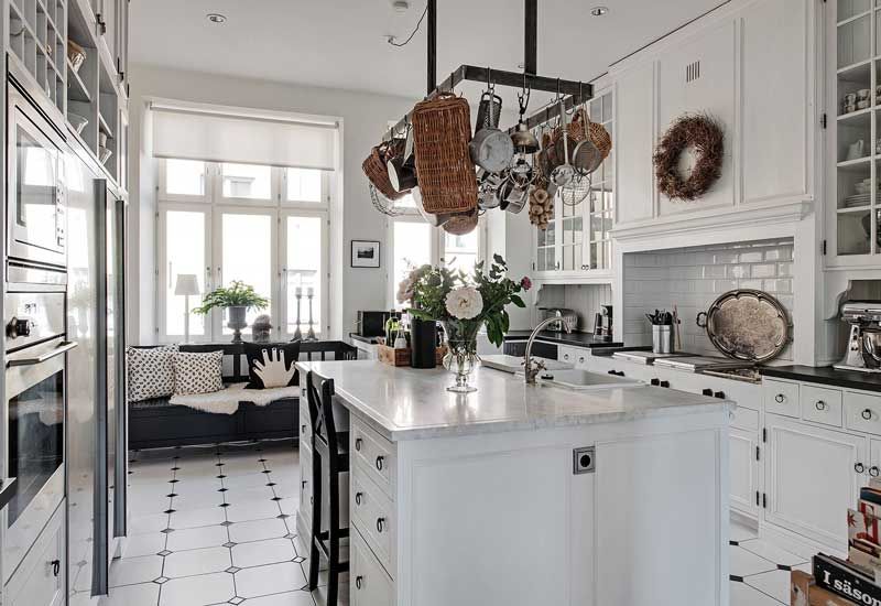 Cocina blanca con isla central con soporte en el techo del que cuelgan cacerolas y accesorios