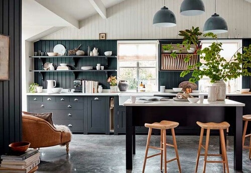 Cocina con muebles negros con tiradores de concha, suelo gris y mesa de 'office' alta con taburetes de madera