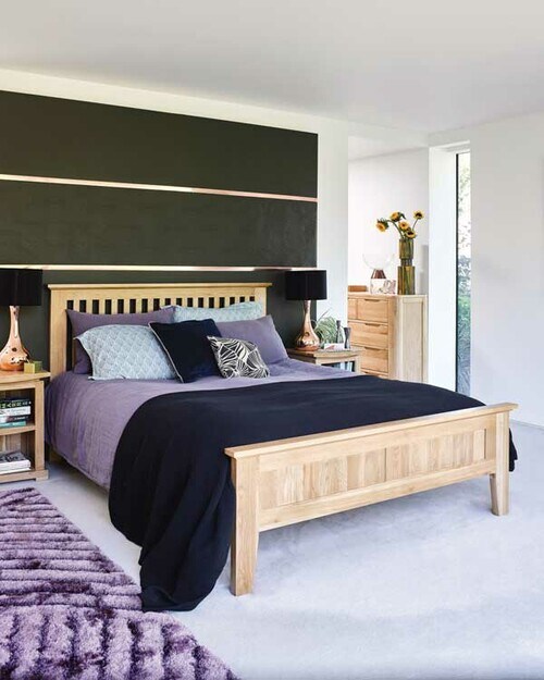 Dormitorio de matrimonio con cama de madera y sábanas y alfombras de color morado 