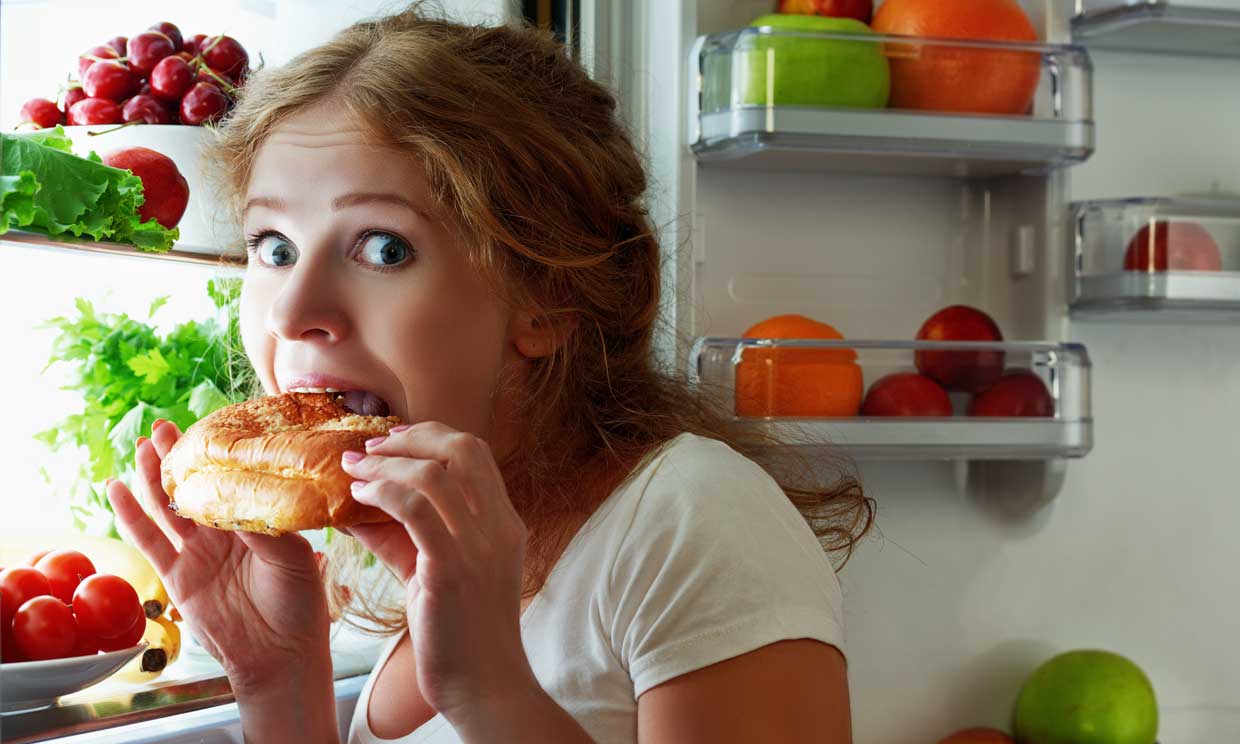 Mujer con sensación de hambre comiendo tras abrir la nevera