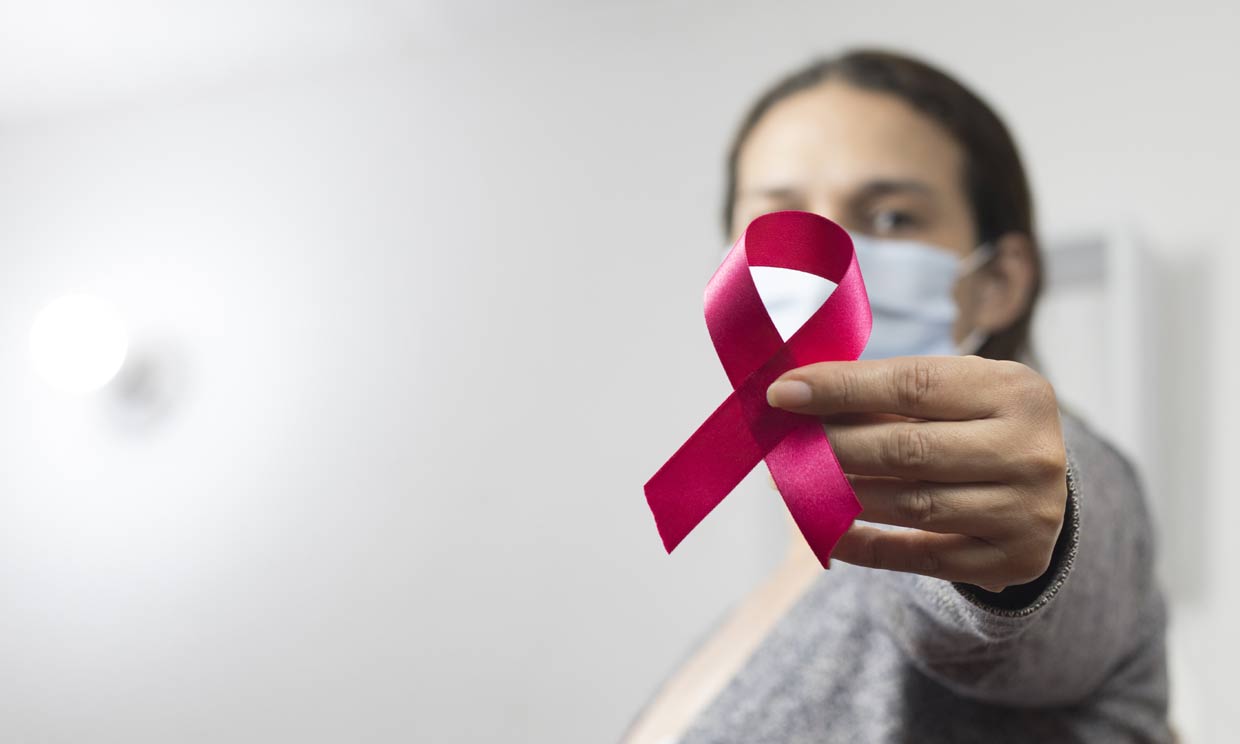 mujer con un lazo de lucha contra el cáncer y mascarilla