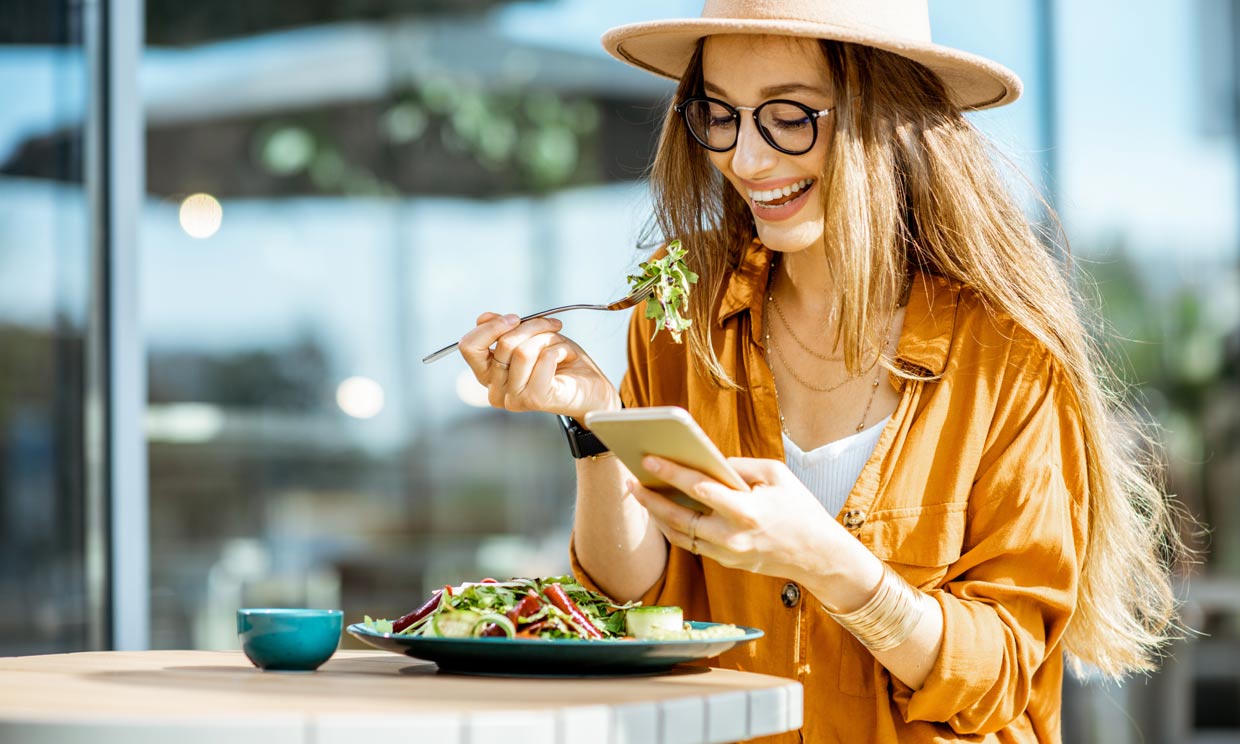 mujer comiendo ensalada mientras mira el móvil