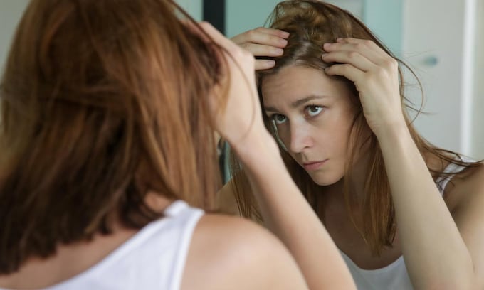mujer mirando su pelo en el espejo