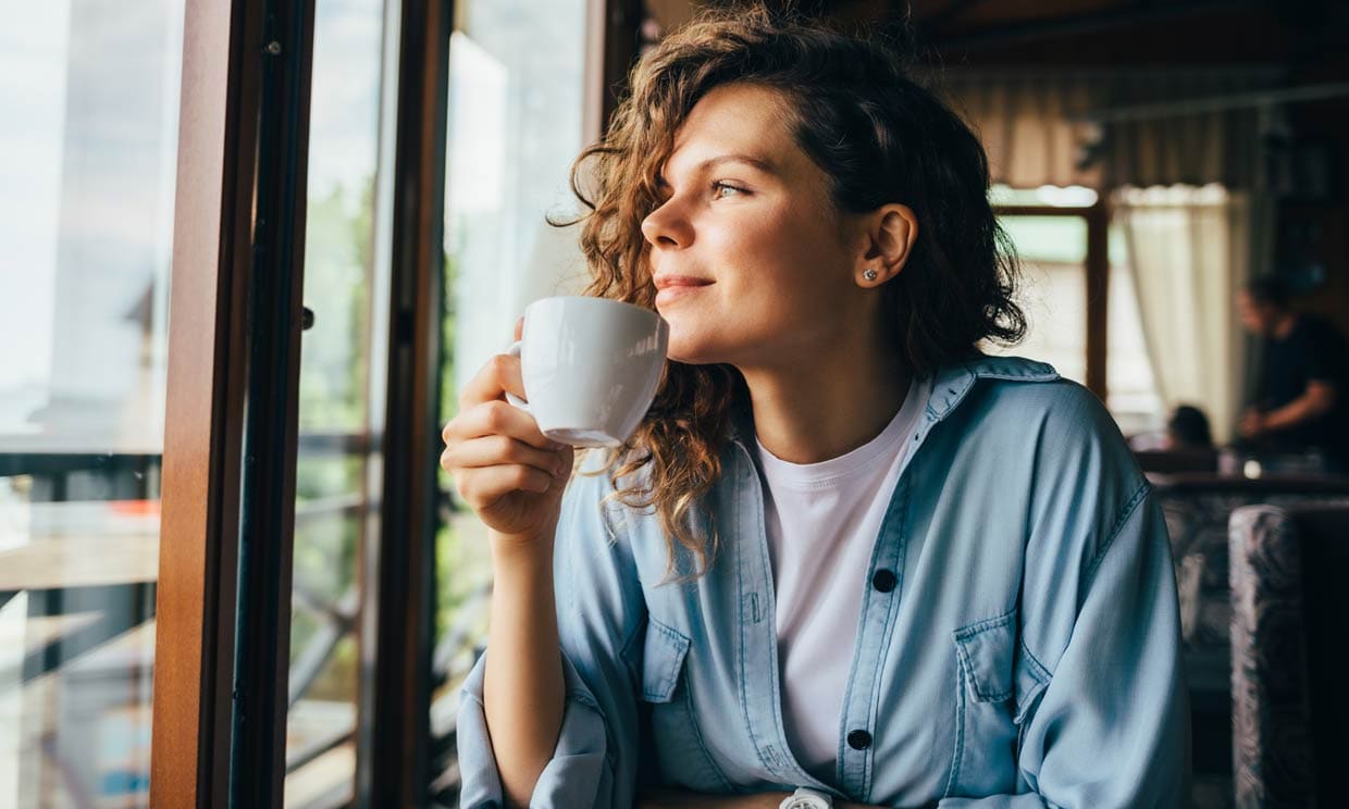 Mujer joven sonriendo, muy tranquila, y tomando un café