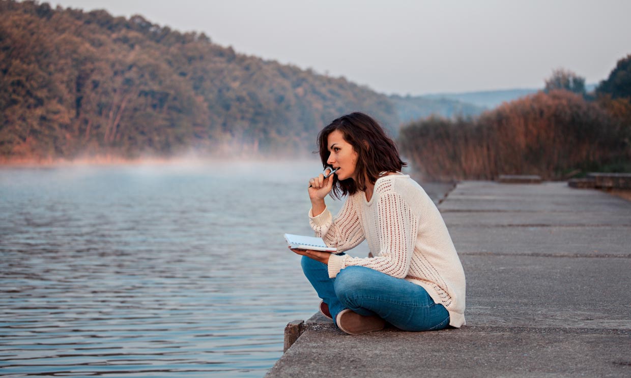 Mujer a la orilla de un lago con un diario en la mano