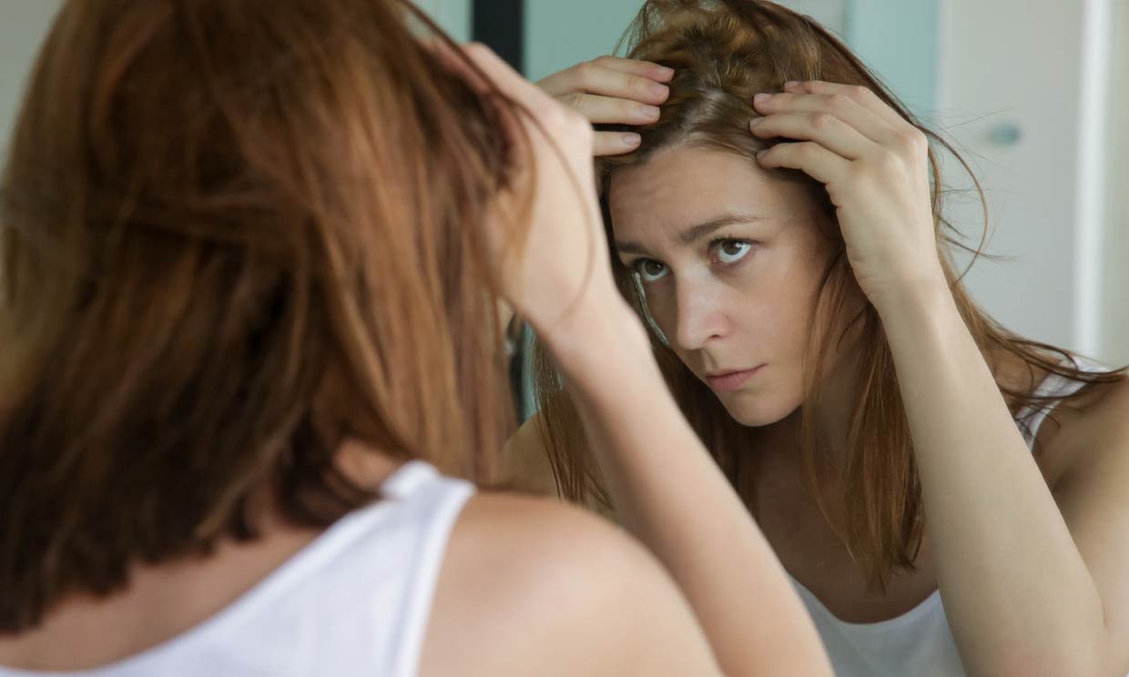 mujer mirando su cuero cabelludo en el espejo