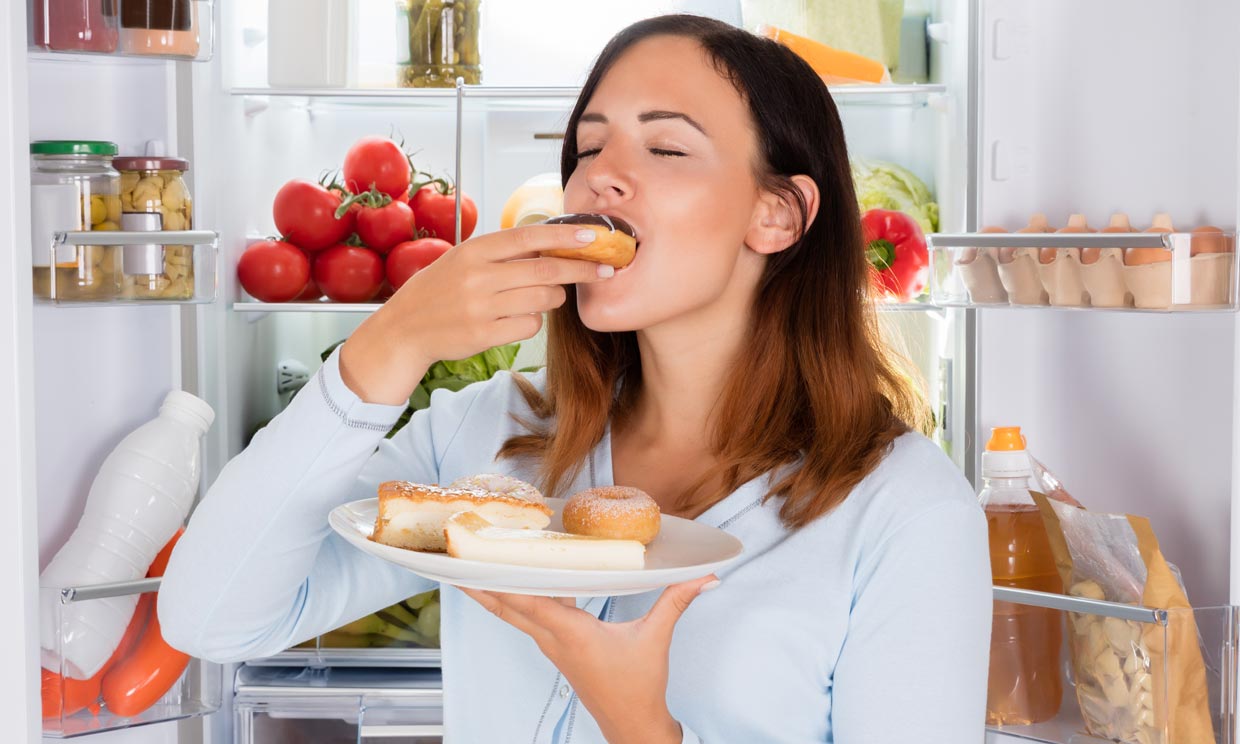 mujer comiendo junto a la nevera