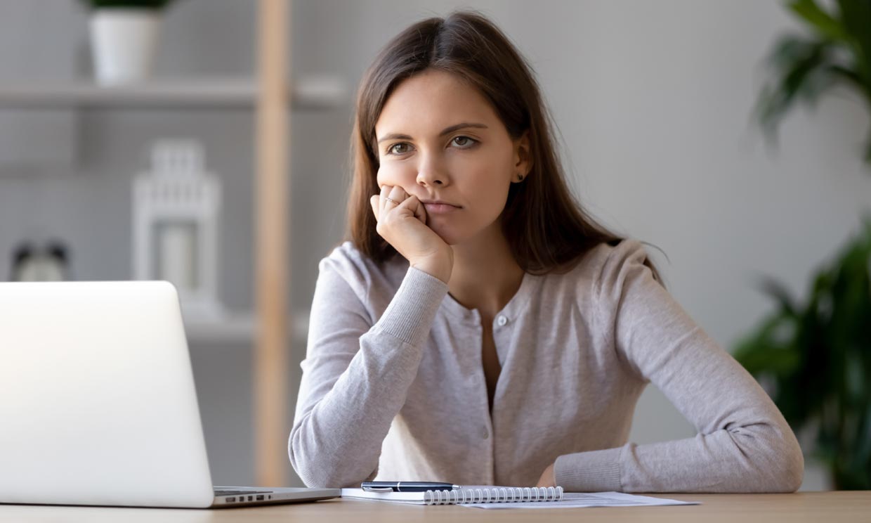 Mujer joven sentada a la mesa, delante del ordenador en actitud apática