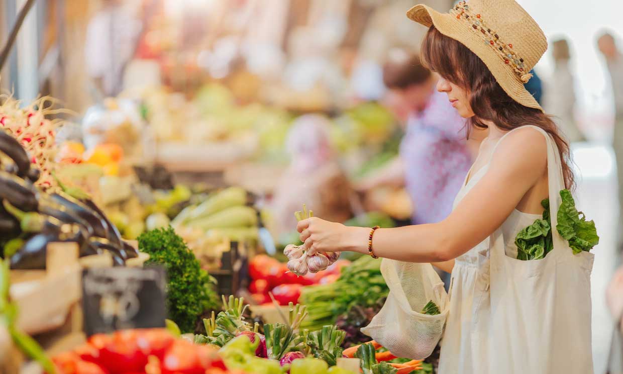 Mujer joven comprando en un mercado con bolsas de tela