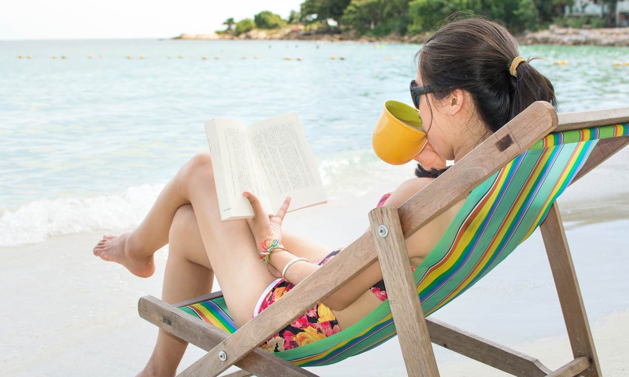 mujer lee y bebe agua en la playa