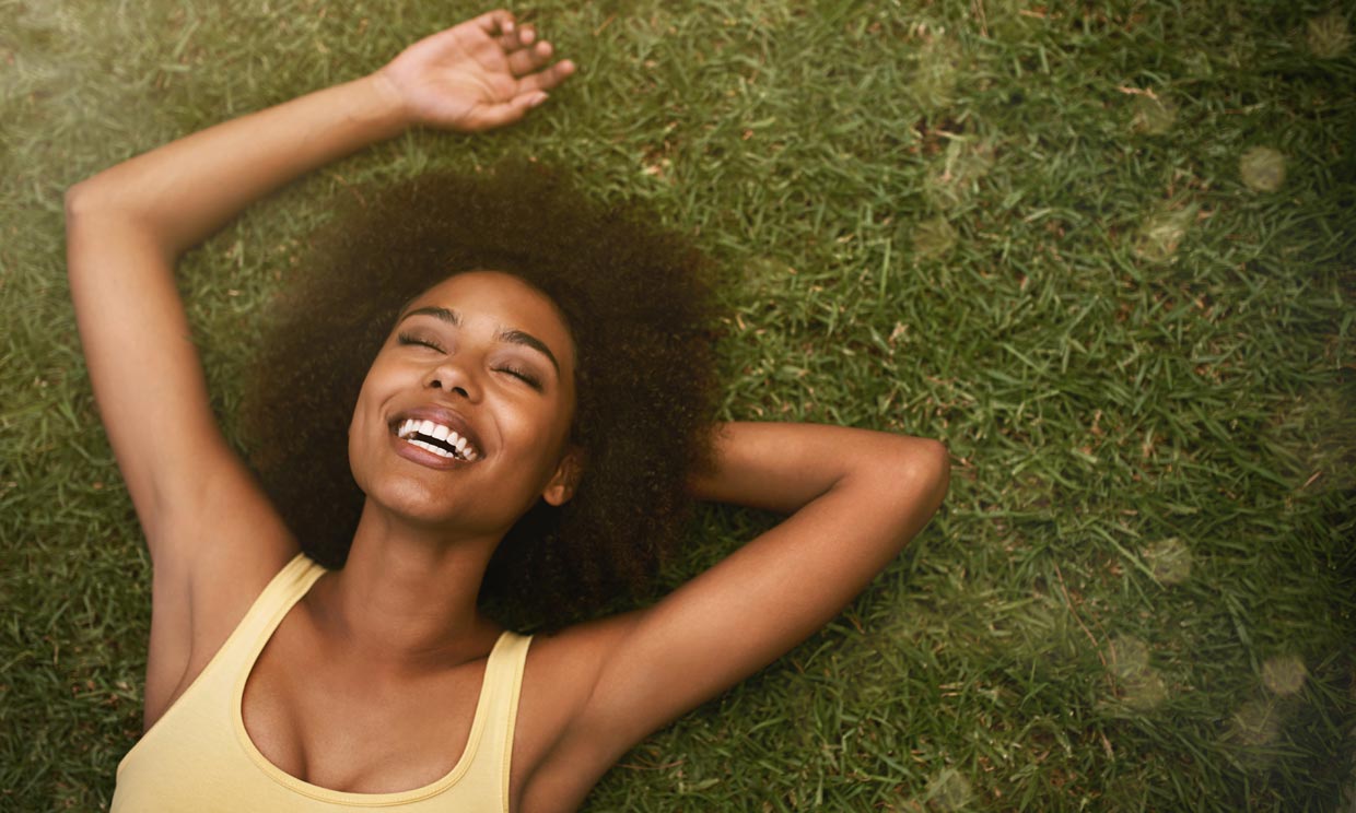 Shot of a young woman laughing while relaxing on the gras