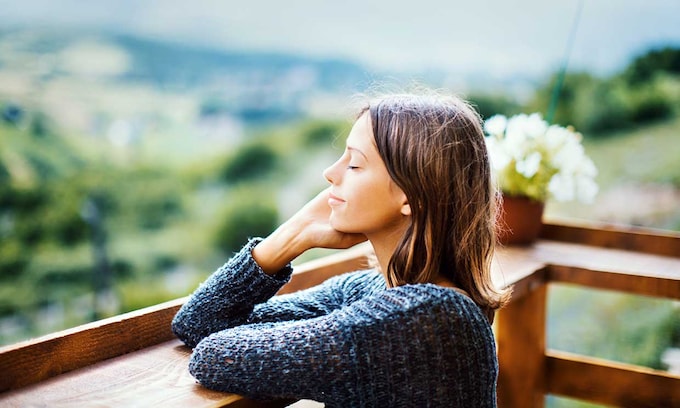 Mujer joven en la terraza de su casa en actitud relajada con los brazos apoyados en la barandilla