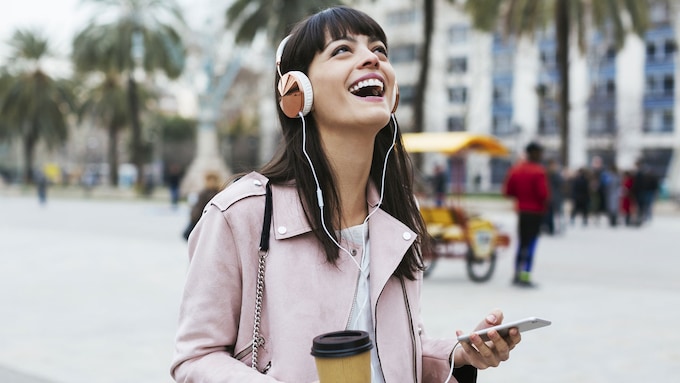 mujer sonriente con auriculares y café en la calle