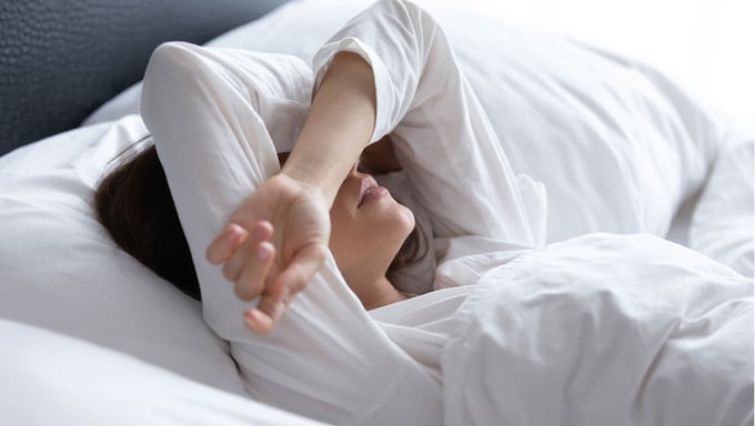 mujer en la cama con la cara tapada por los brazos