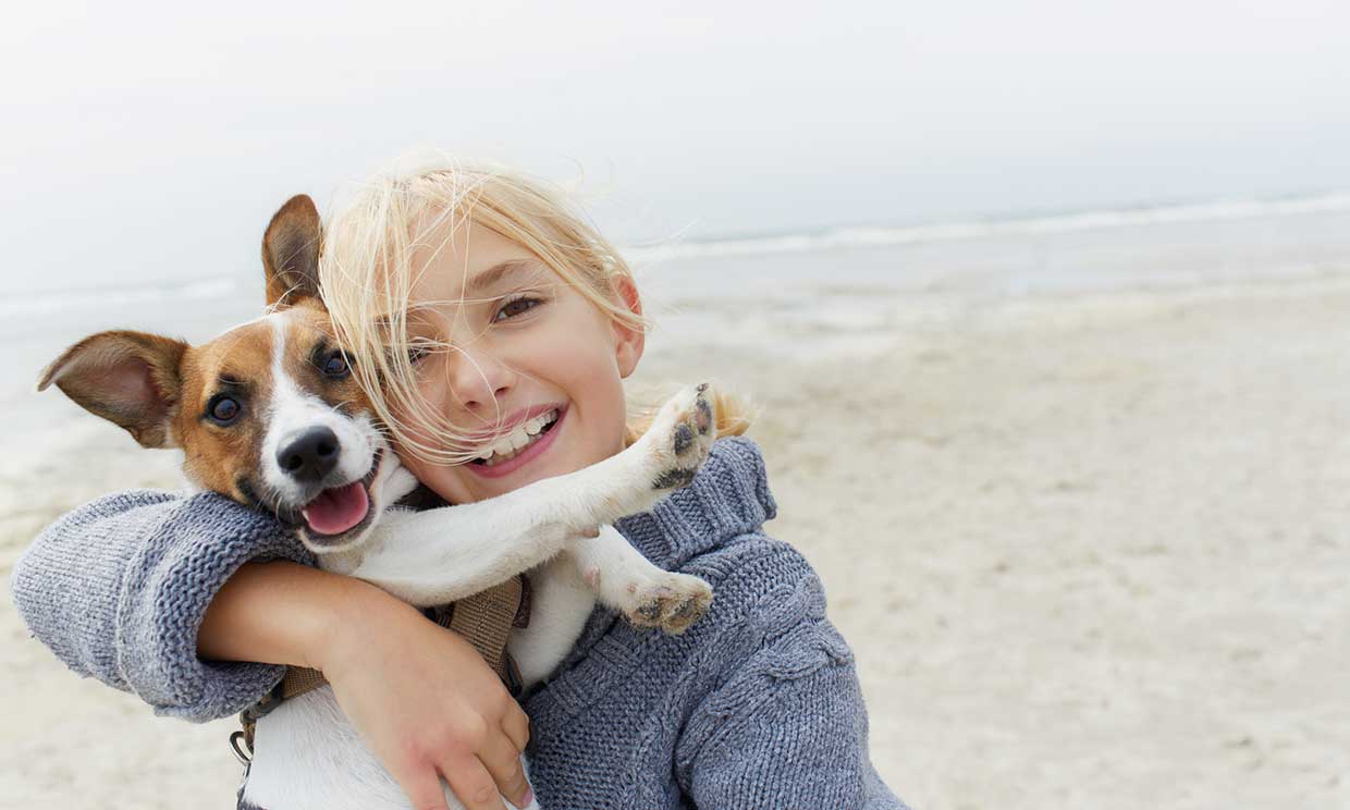 Niña abrazando a su perro en la playa