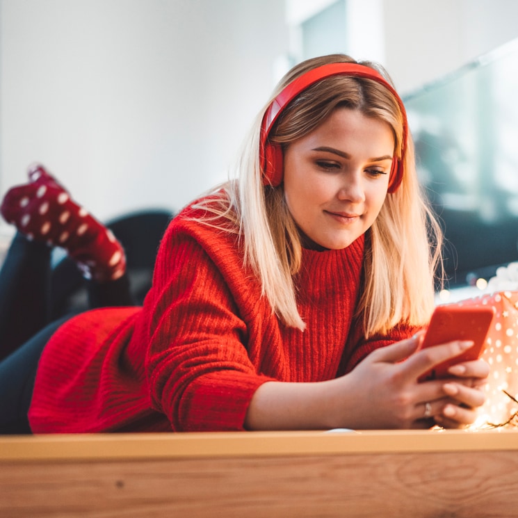 Chica universitaria con cascos y teléfono móvil rojos en Navidad