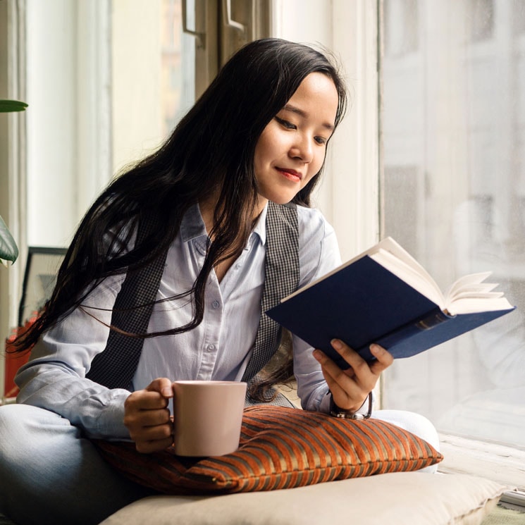 Mujer leyendo un libro junto a la ventana