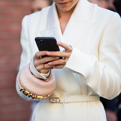 Caroline Daur con blazer blanca mirando su teléfono movil