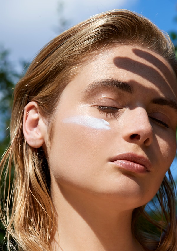 Mujer aplicándose crema facial solar en el rostro