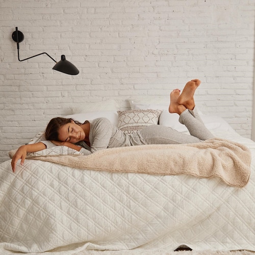 Coco Constans dormida en una cama con sábanas y colcha de Textura Interiors