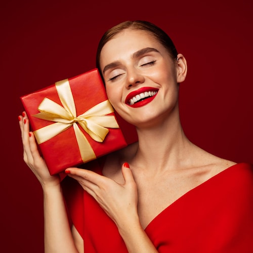 Mujer con vestido, uñas y labios rojos sosteniendo un regalo