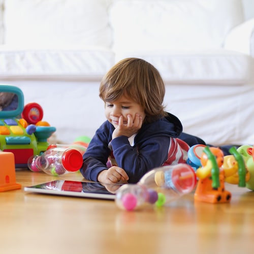 Niño tumbado en el suelo rodeado de juguetes mirando una tablet