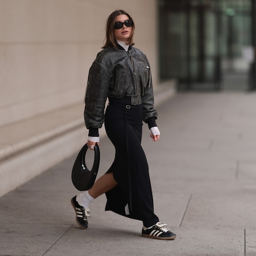 Mujer caminando por la calle con falda, cazadora de cuero y zapatillas de Adidas