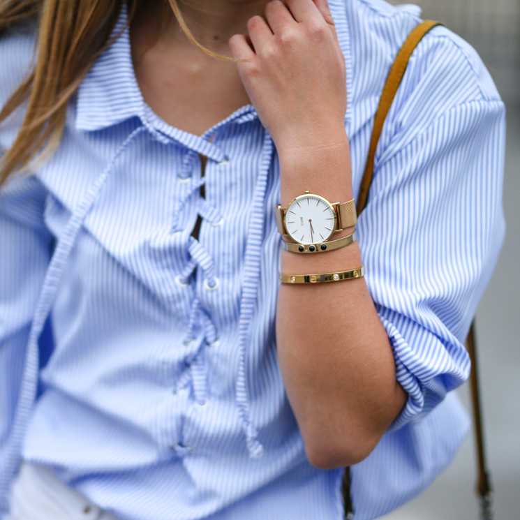 Mujer con reloj de pulsera dorado, brazaletes y camisa de rayas