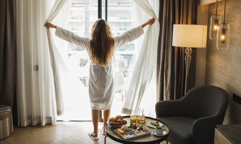 Mujer abriendo las cortinas de la habitación del hotel