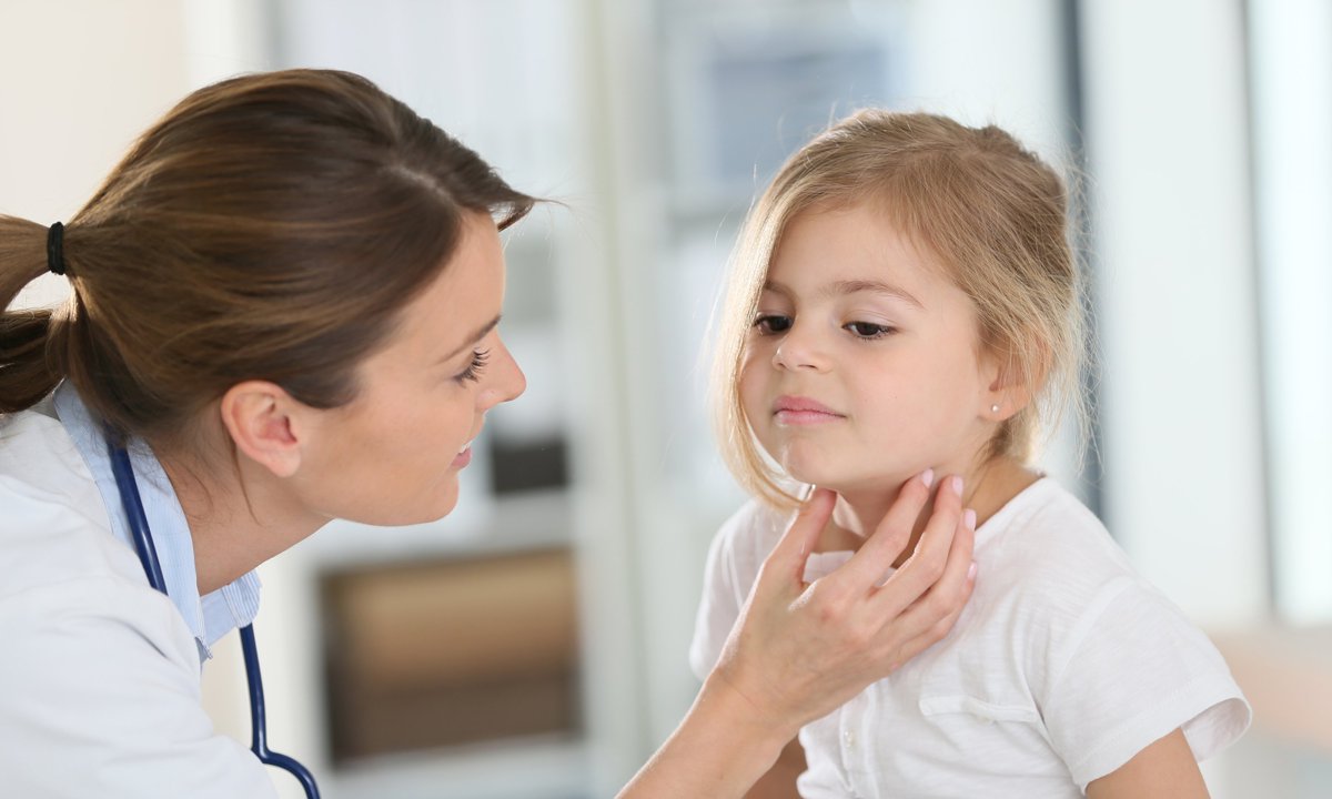 Niña pequeña en la consulta del pediatra para exploración de la garganta