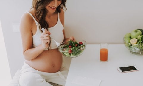 Mujer embarazada comiendo saludable en la cocina.