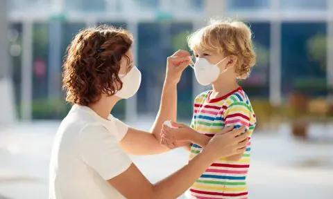 Madre poniéndole a su hijo la mascarilla en la calle.