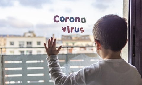 Niño mirando por una ventana donde se puede leer coronavirus