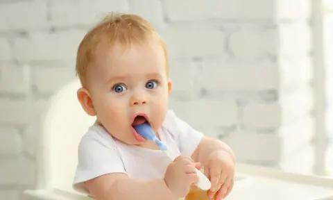 Bebé sentado en una trona con una cuchara en la boca