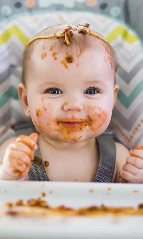 Bebé manchado de tomate comiendo en una trona